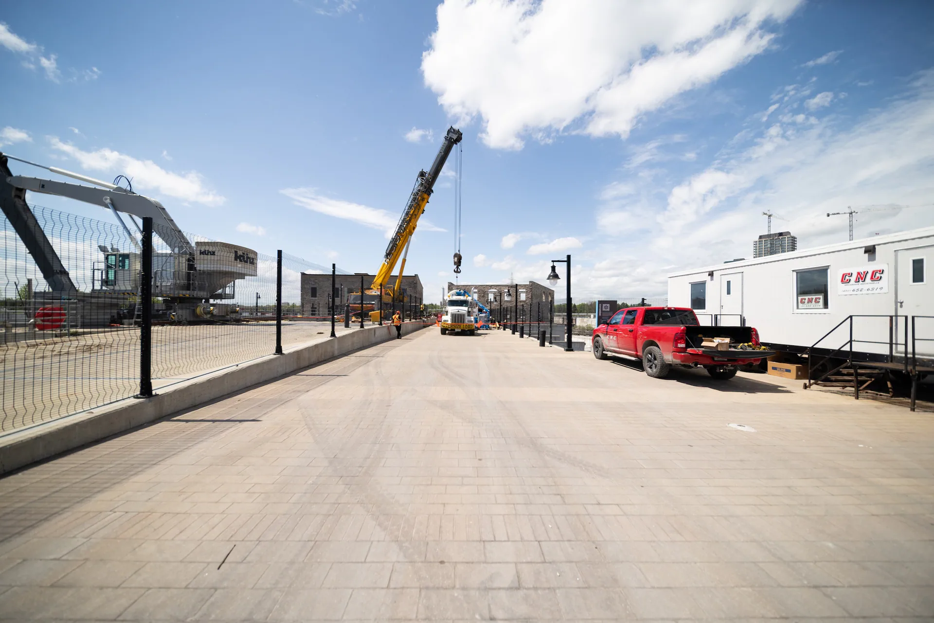 Wide CNC-branded worksite with a trailer, pickup, mobile crane and heavy transport equipment.