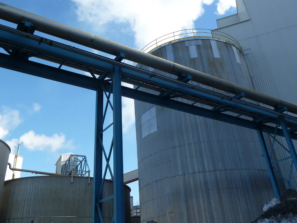 Blue inclined conveyor gallery rising toward a storage tank.