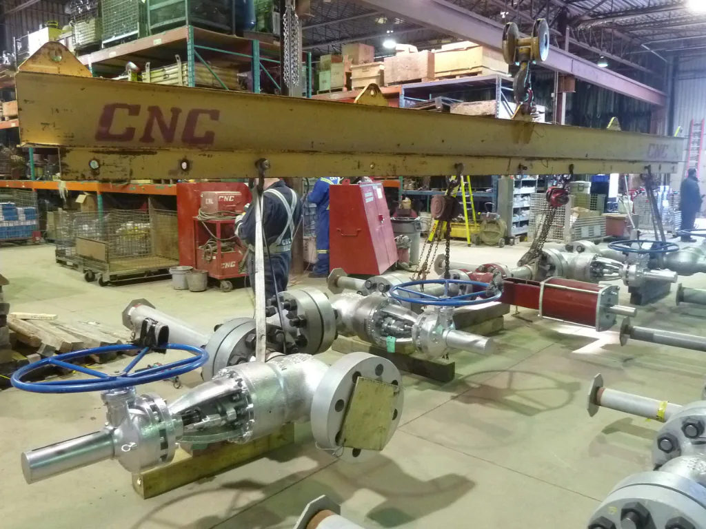 Valve and piping assemblies in a shop, beneath an overhead crane marked CNC.