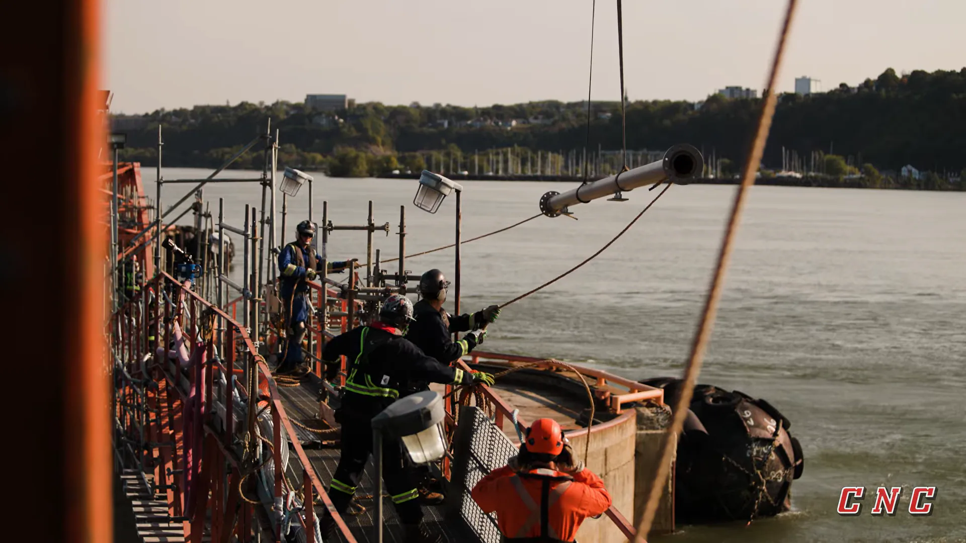 Workers guiding a suspended pipe section over Valero’s wharf in Lévis.