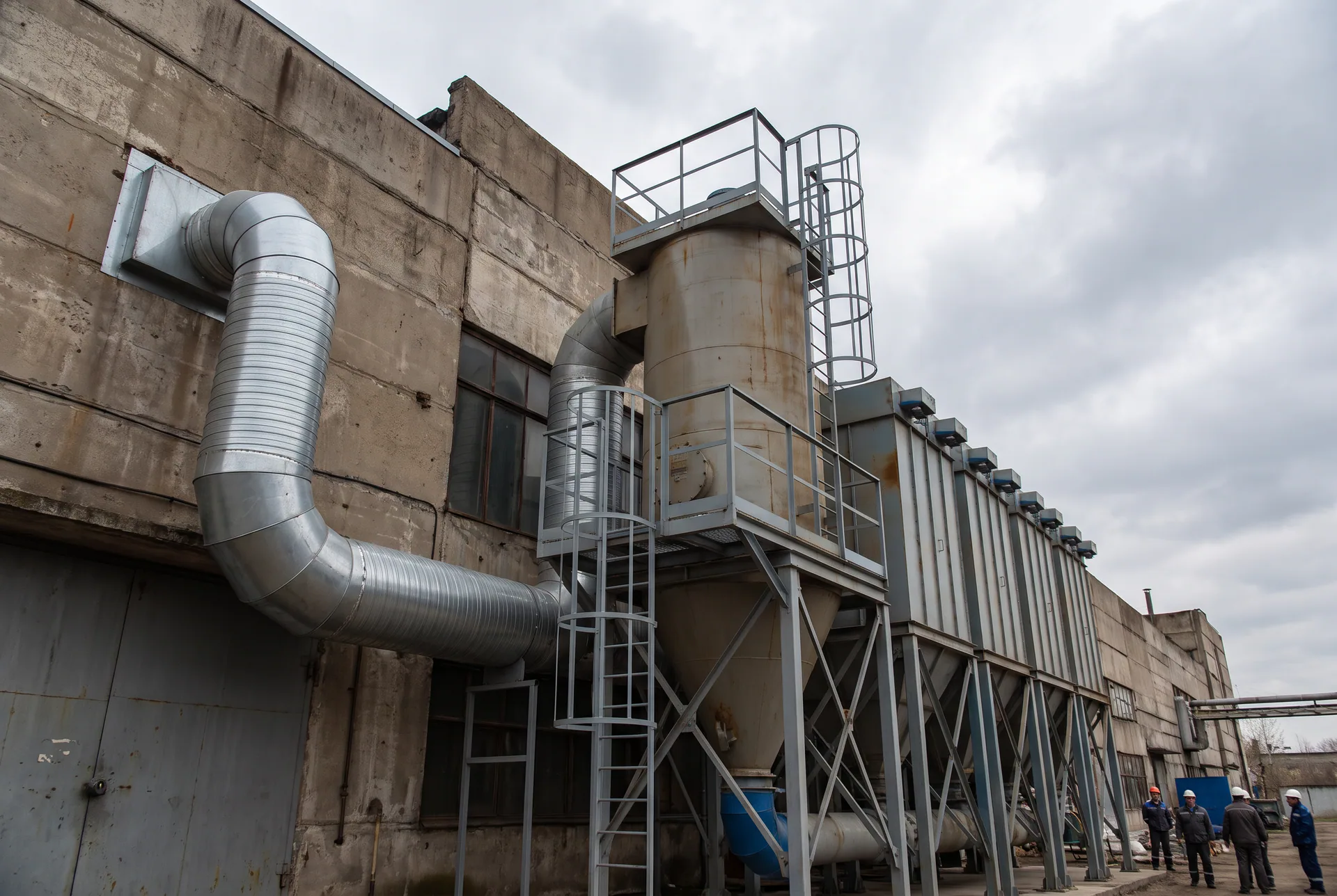 Generic industrial dust collection system: baghouse collector, hopper and spiral ductwork along a building, with no identifiable client or facility.