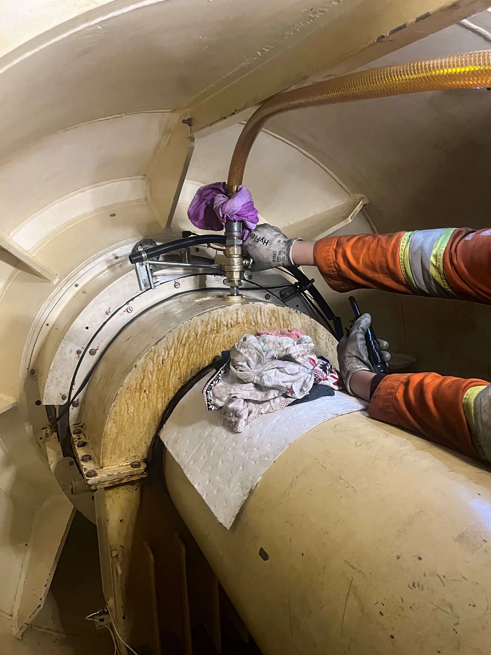 Close view of gloved hands operating a hydraulic tool and hoses on a circular industrial machine assembly.