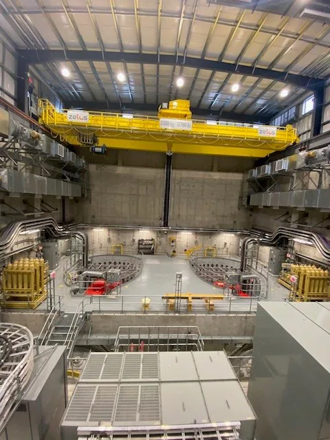 Wide interior of a large powerhouse-like hall with two yellow overhead bridge cranes and machinery bays.