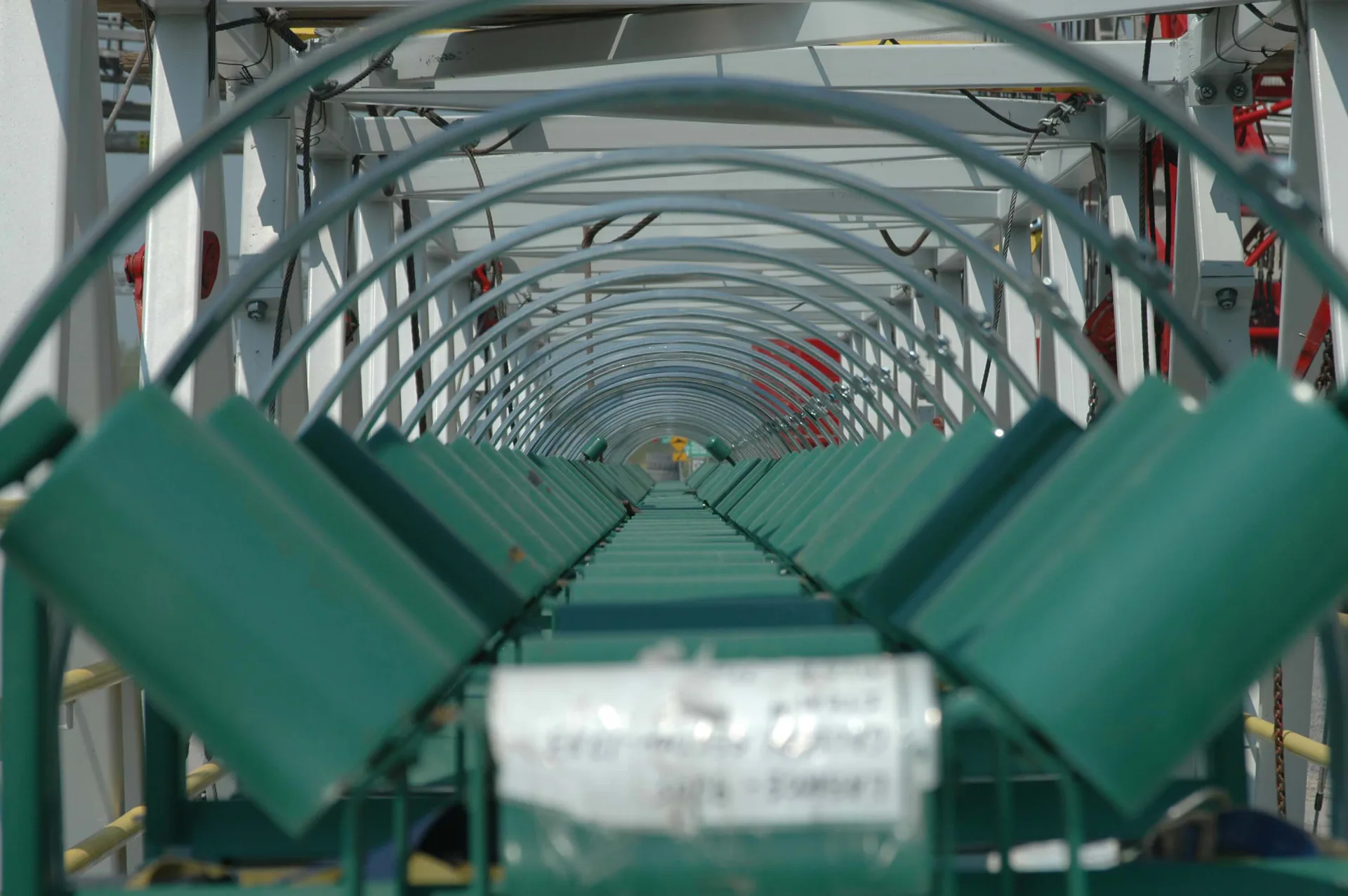 Close perspective along green conveyor idler rollers beneath repeated arched guards.
