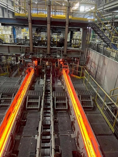 Interior production line showing two glowing hot steel strands moving through rollers.